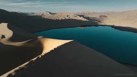 A shadowed dune crest curving down to a still teal desert lake.