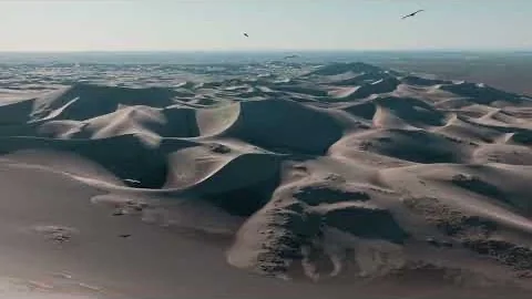 Desert dunes from high altitude, each crest throwing a long raking shadow.