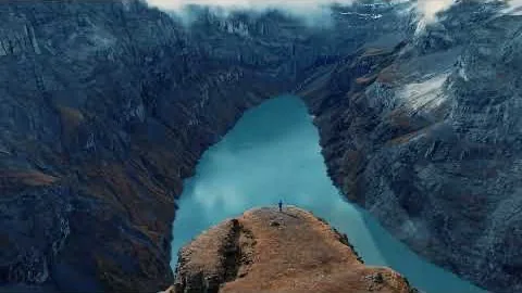 A rust-coloured ridge spur reaching into a turquoise glacial lake, one figure at its tip.