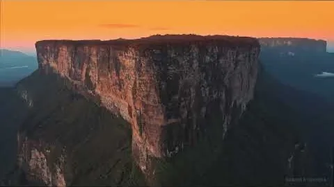 A sheer-walled table mountain lit orange along its rim by a low sun.